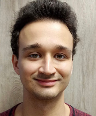 The image shows a person with short hair, wearing a dark shirt, smiling at the camera.