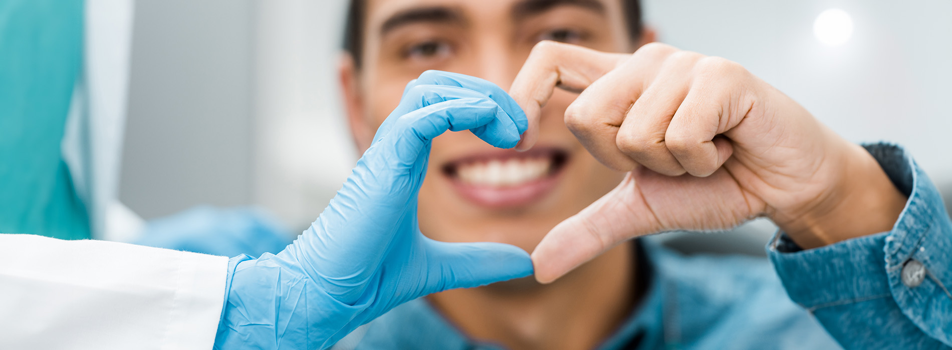 The image shows a person making a heart shape with their hands, standing behind a pair of blue gloves, with a smiling face visible from the back, and they are wearing a lab coat, suggesting a medical or scientific setting.