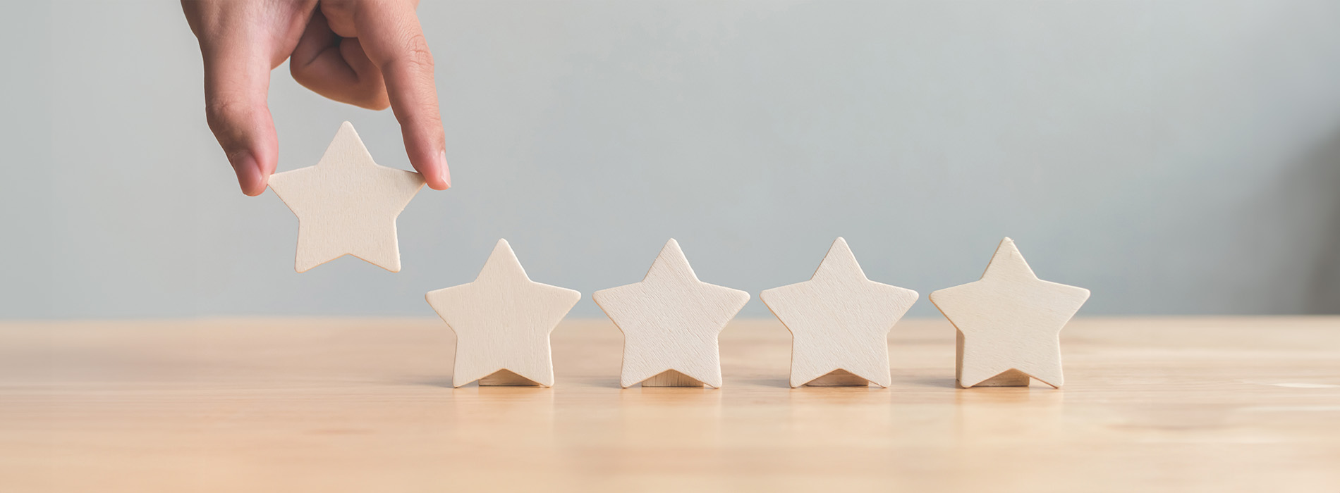 The image shows a person s hand holding wooden star-shaped objects against a blurred background with a focus on a white surface, suggesting a crafting or decoration activity.