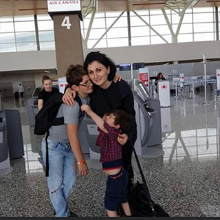 The image shows a woman and two children at an airport check-in counter, embracing each other with luggage around them, seemingly waiting for their flight.