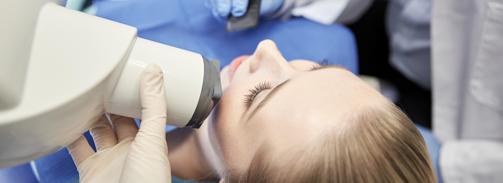 The image shows a person receiving dental treatment with a dentist using a microscope.