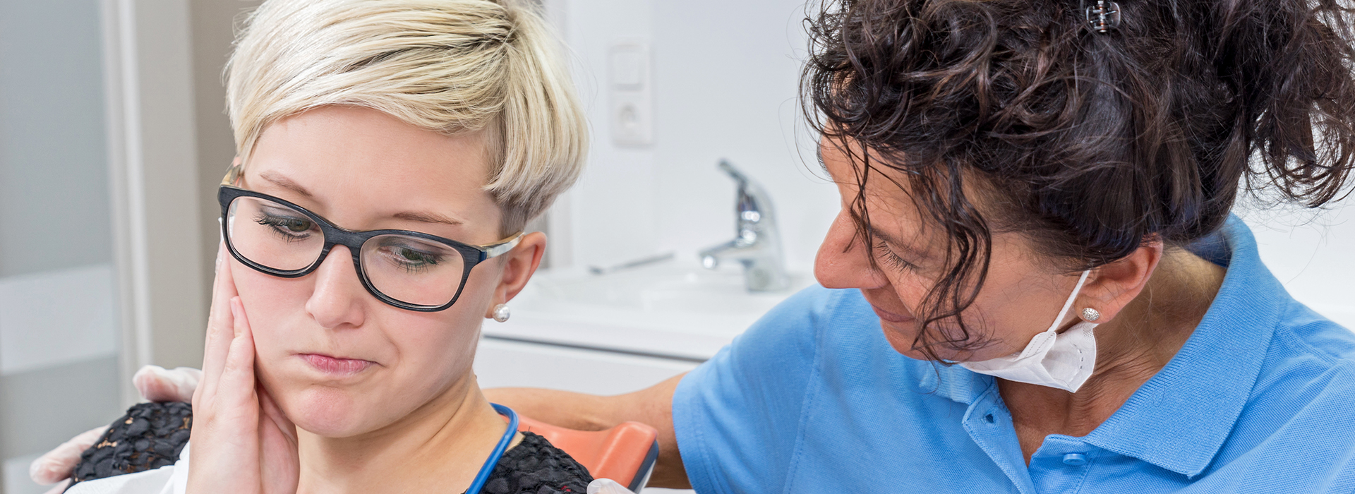 A woman with glasses is being examined by a dental hygienist in a dental office setting.