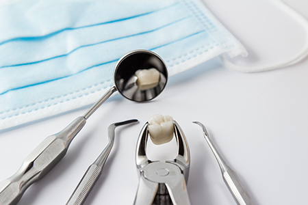 The image displays a collection of dental tools including a drill, a scaler, and a small toothbrush, all placed on a white background with a blue surgical mask partially visible at the bottom left corner.