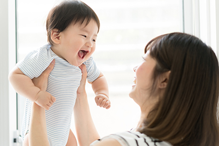 A woman holding a baby who is smiling and looking upwards.