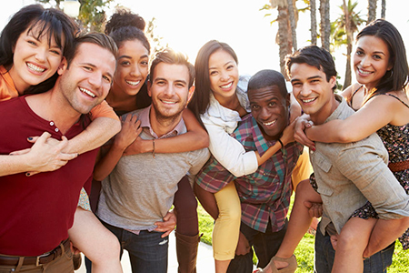A group of six people posing together with smiles on their faces, standing outdoors during daylight.